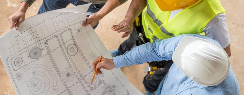 Group of civil engineers looking at blueprints at a construction site and wearing helmets